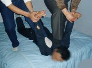 酷刑演示：掰，下巴擔在床上，惡人再把受害人兩手反背後面使兩腿翹起