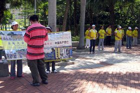 圖：中國大陸遊客在法輪功真相展板前細看內容（右邊是學員每日的晨煉）