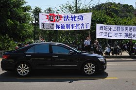 「你被刑事控告了」──安徽省省長王三運四月二十日上午至桃園縣桃園銘傳大學時，車隊在校園路前看到法輪功學員的抗議橫幅