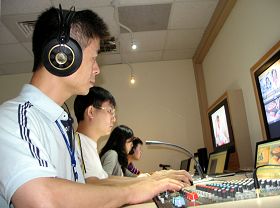 阿亮（前一）在新唐人亞太台負責成音部份。他正為晚間新聞播出的音控工作。