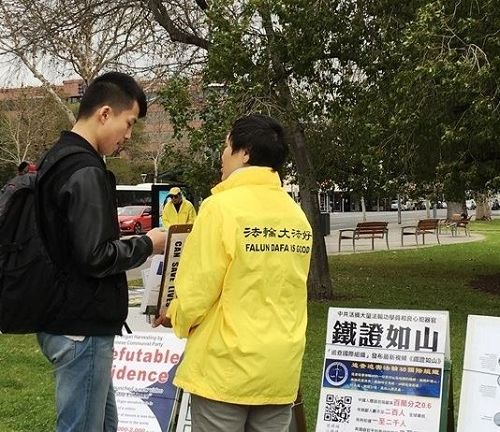 '圖5：來自中國大陸的年輕人，在真相展板前駐足良久，聆聽法輪功學員講述真相，最後欣然用化名退出了中共的團、隊組織。'