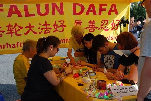 '圖5：遊客們在法輪功的展位上學習折蓮花。'
