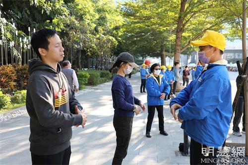 '圖13：盧女士（中）正在活動現場旁學煉法輪功。'